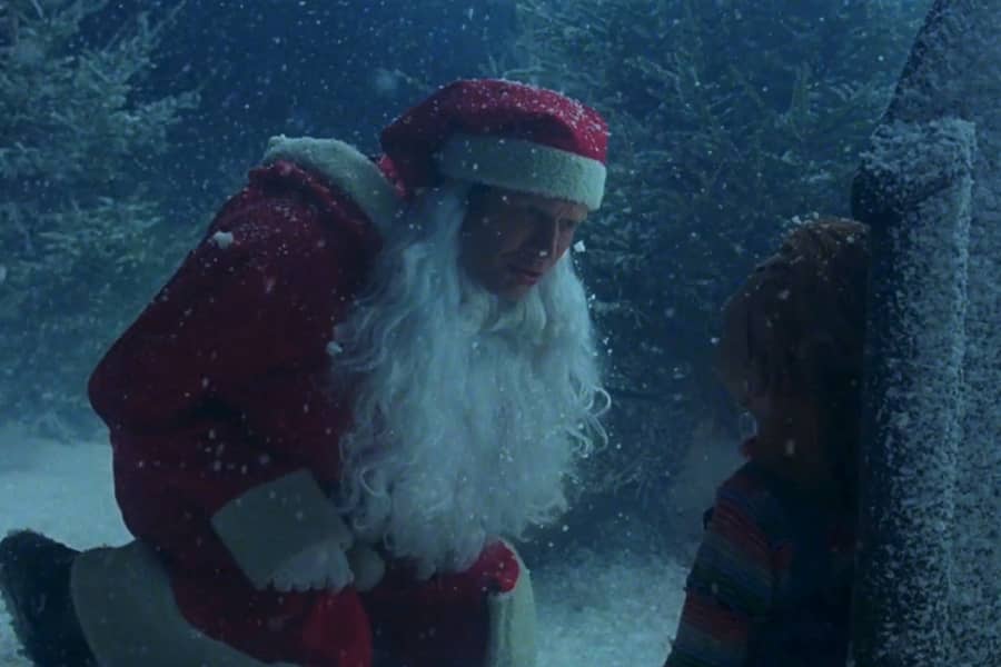 Santa man leans in to inspect a doll leaning on a gravestone