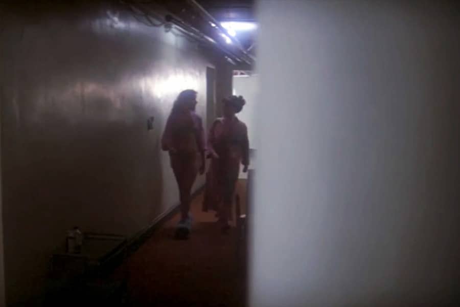 peering around a corner at two women walking down a hallway