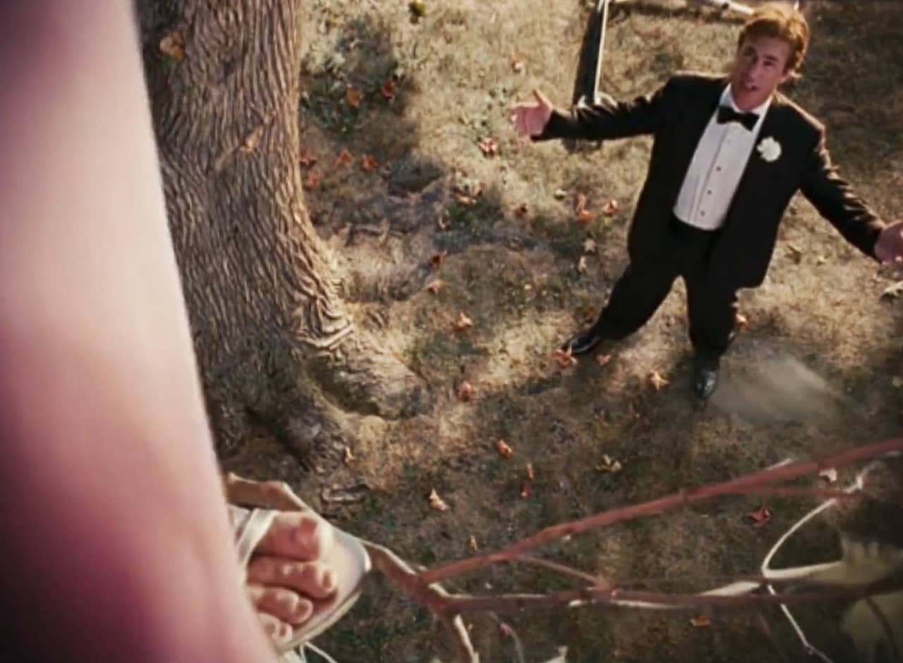 an exasperated man in a tux speaks to a woman in a tree