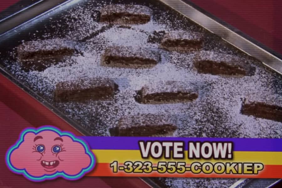 tray of log-shaped, chocolate cookies dusted in powdered sugar with a Vote Now and phone number chyron