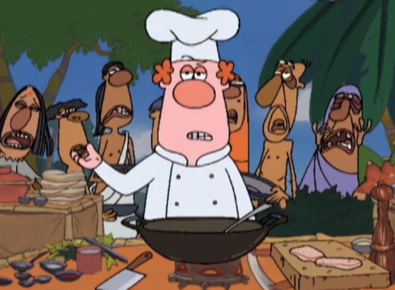 Peter Fish in chef’s clothes in front of a wok, unhappy looking Indian people standing behind him