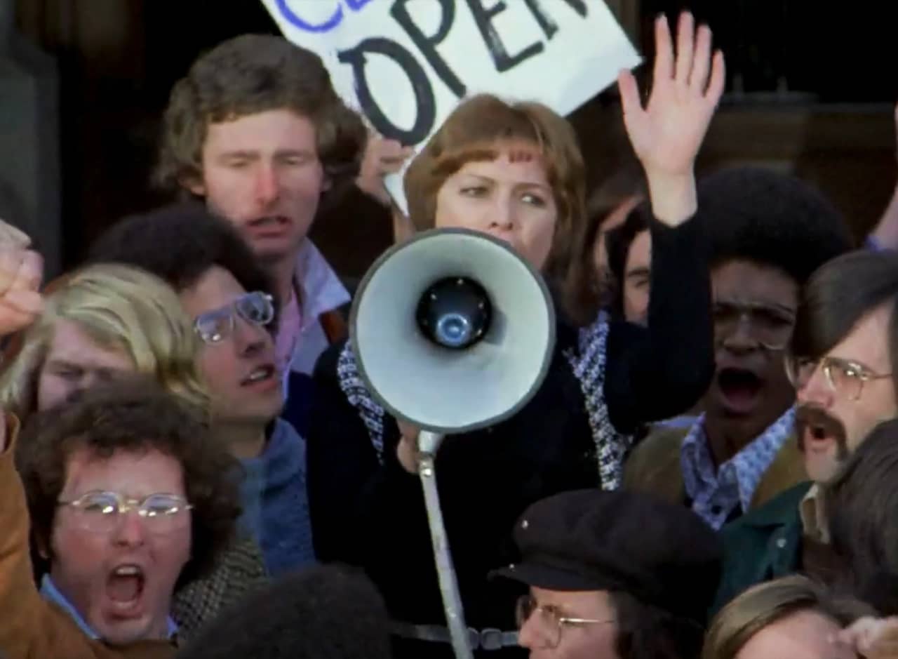 a woman speaks on a megaphone in a crowd of protestors