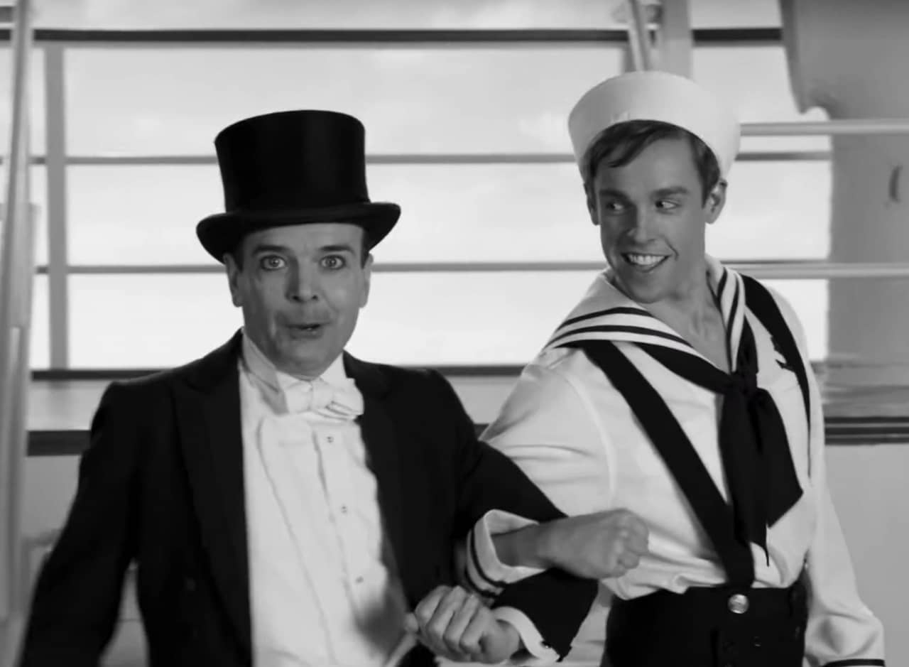 black and white classic film: a young sailor walks arm in arm with an older fancy gentleman