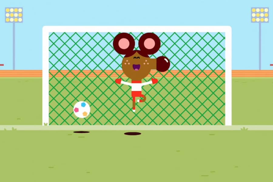 girl playing goalie, singing and dancing, while the ball is going into the net