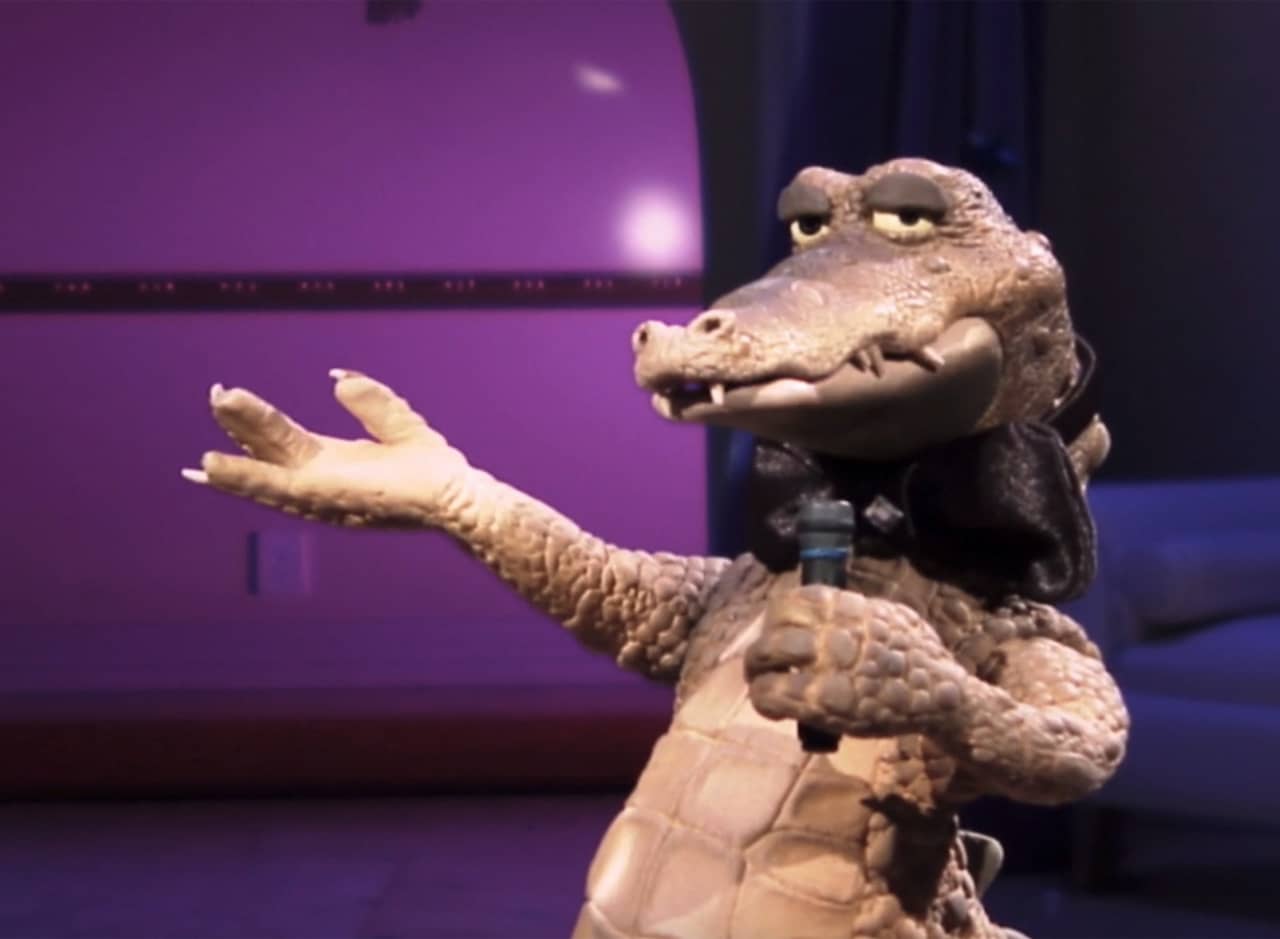Rico the crocodile wearing a bowtie and holding a microphone