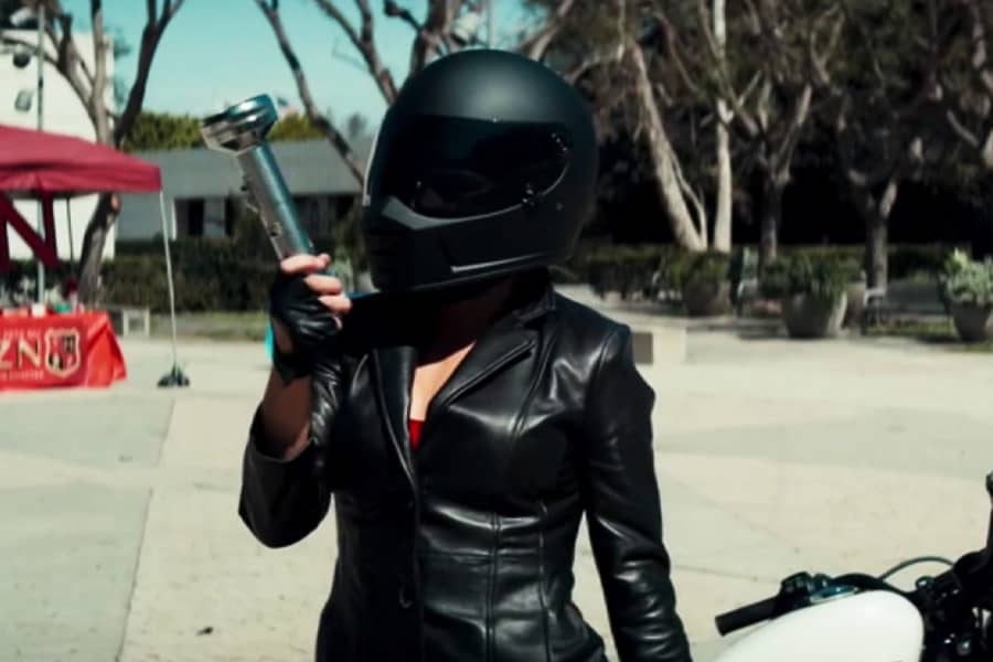 a woman in a motorcycle jacket and helmet holds up a silver flashlight