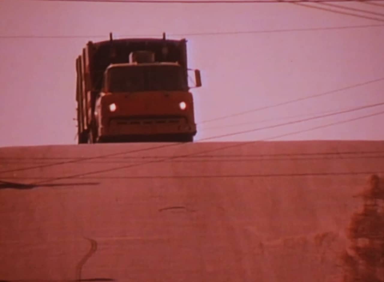 a garbage truck approaching from over a hill