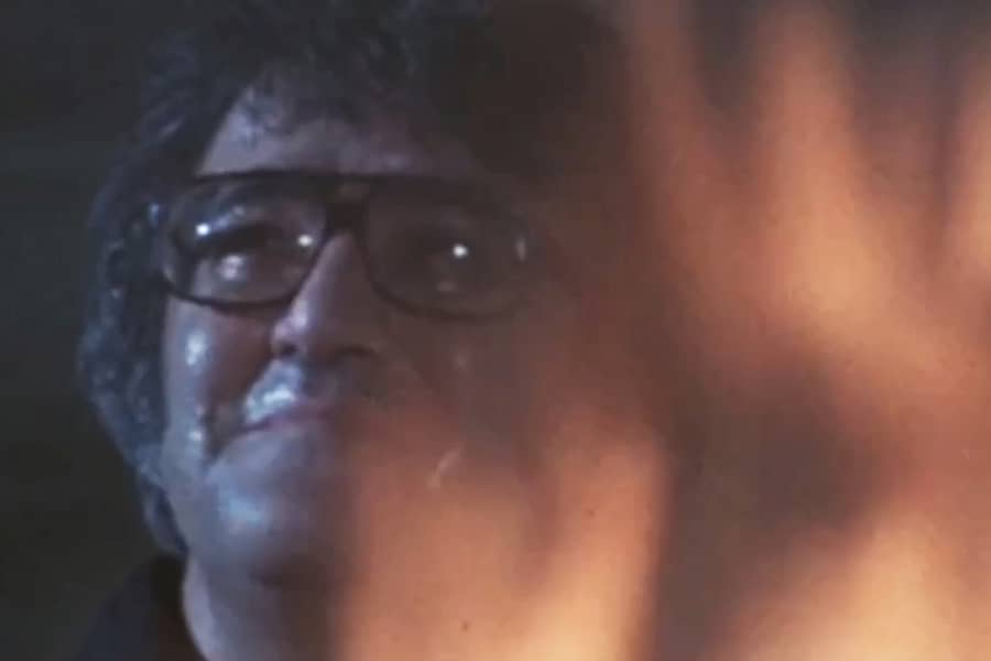 a man with glasses reflects as flames rise up around him