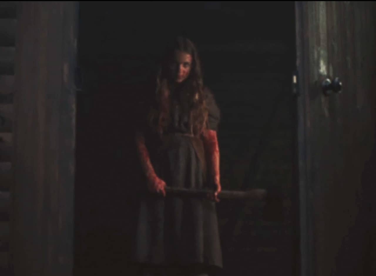 girl holding an axe in the doorway of a cabin