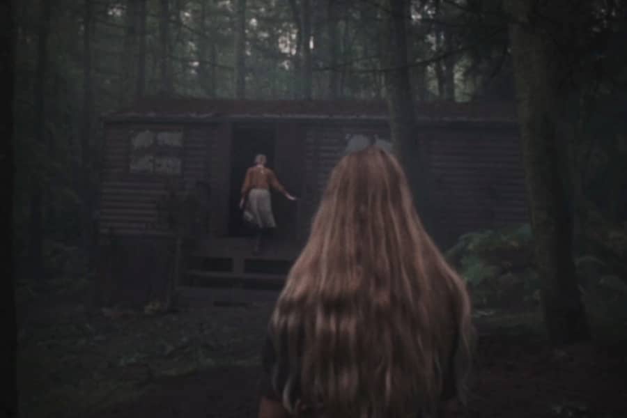 girl watches her sister go into a cabin in the woods