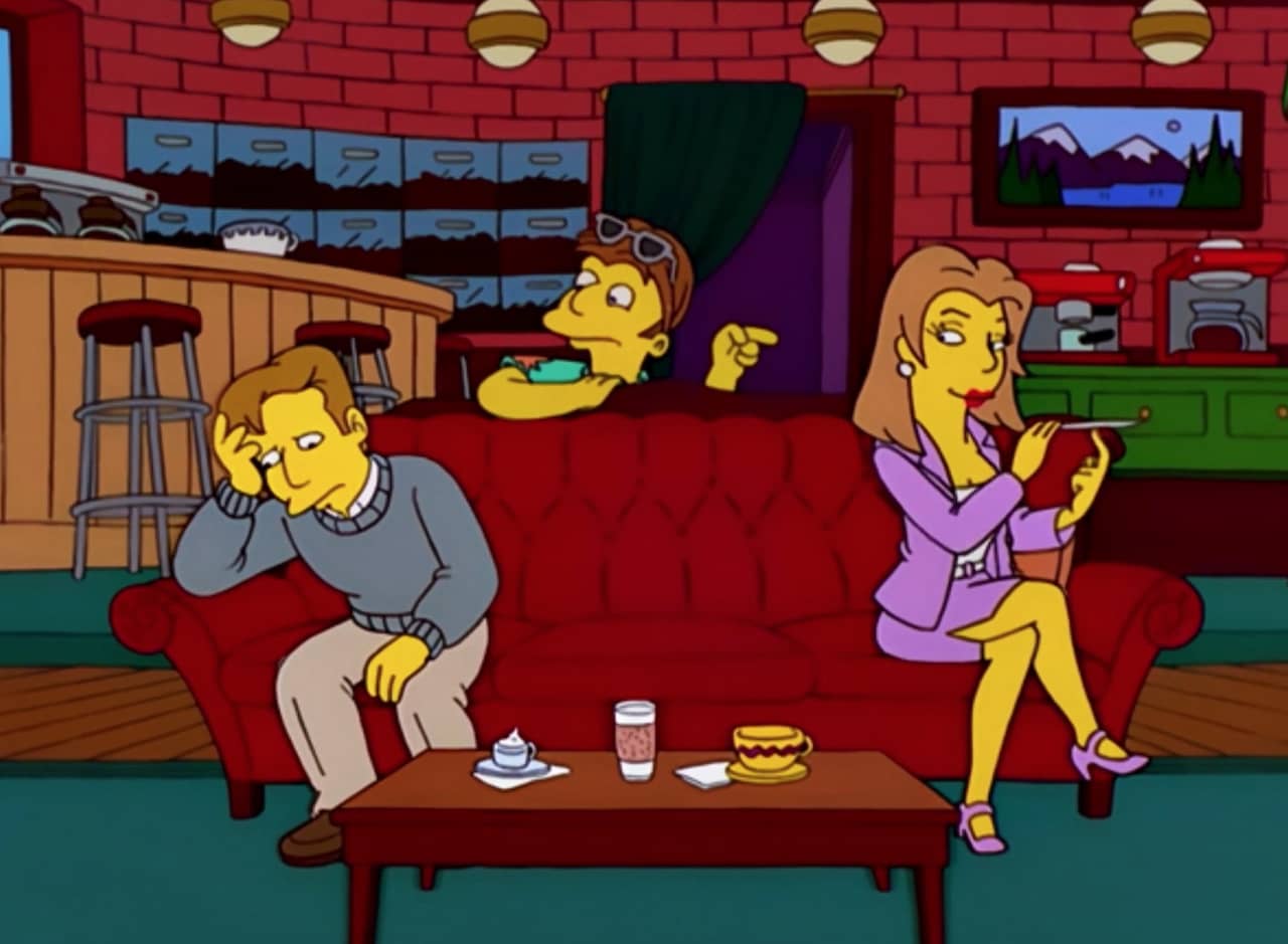 group of friends sitting on a couch in a coffee shop: one guy looks embarrassed, one guy is pointing at the woman who is filing her nails