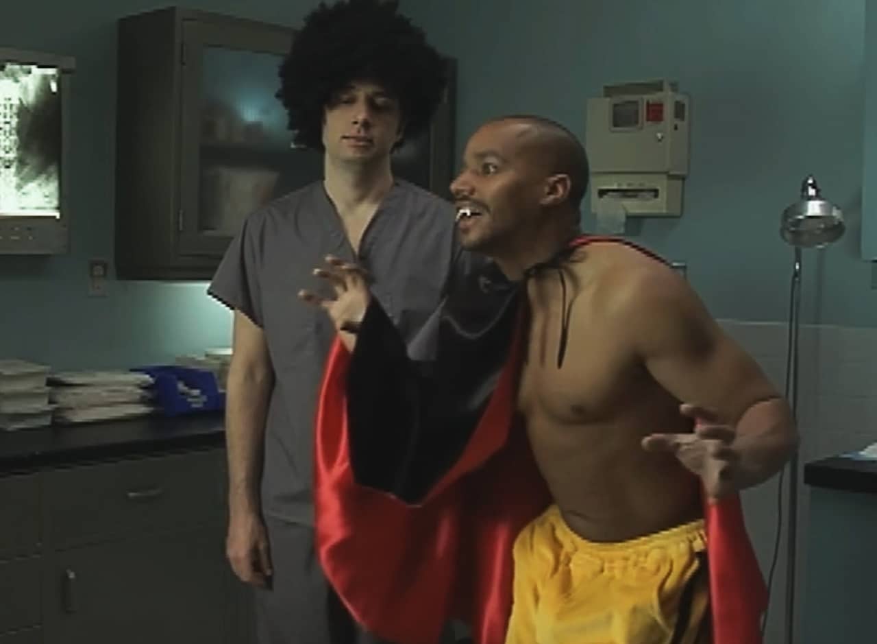 JD in scrubs wearing an afro wig, Turk shirtless wearing a vampire cape and fake teeth