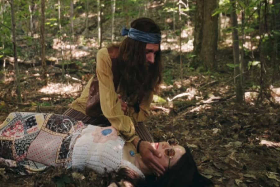 hippie man leaning over dead woman putting his hand on her face
