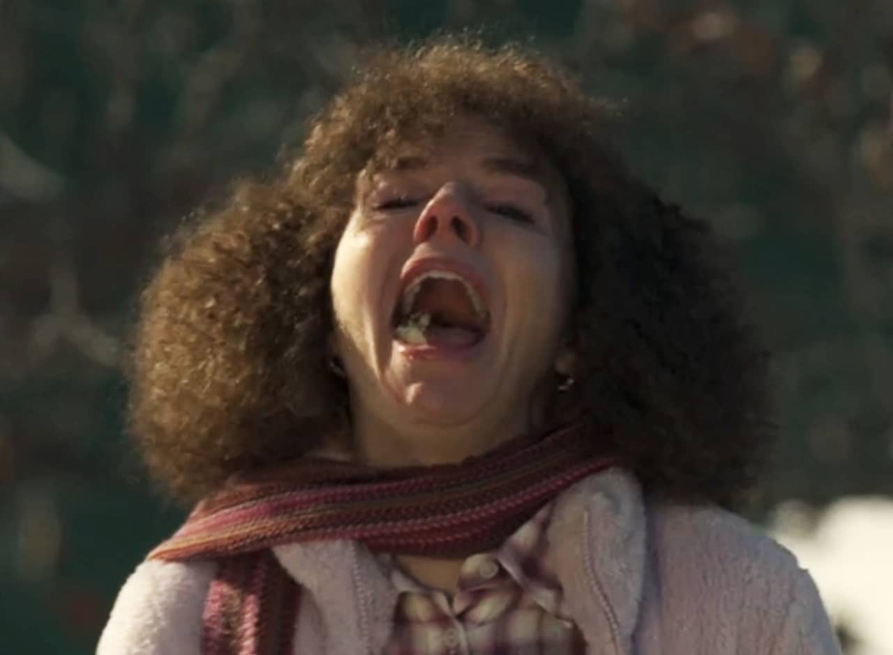 woman with brown curly hair screams with chunks of fruit in her mouth