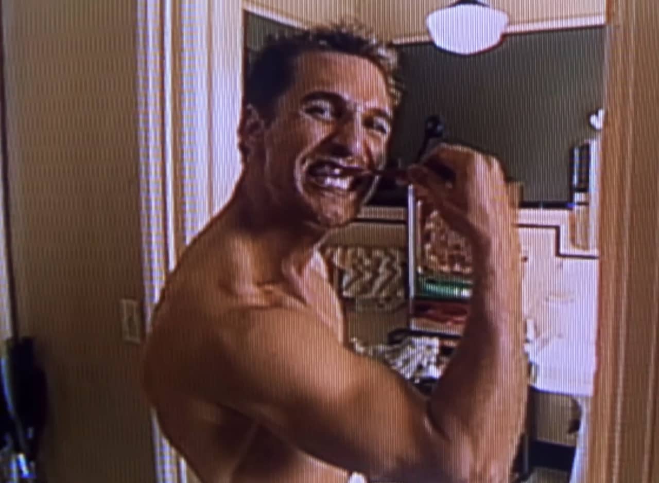 Ed, shirtless and flexing while brushing his teeth