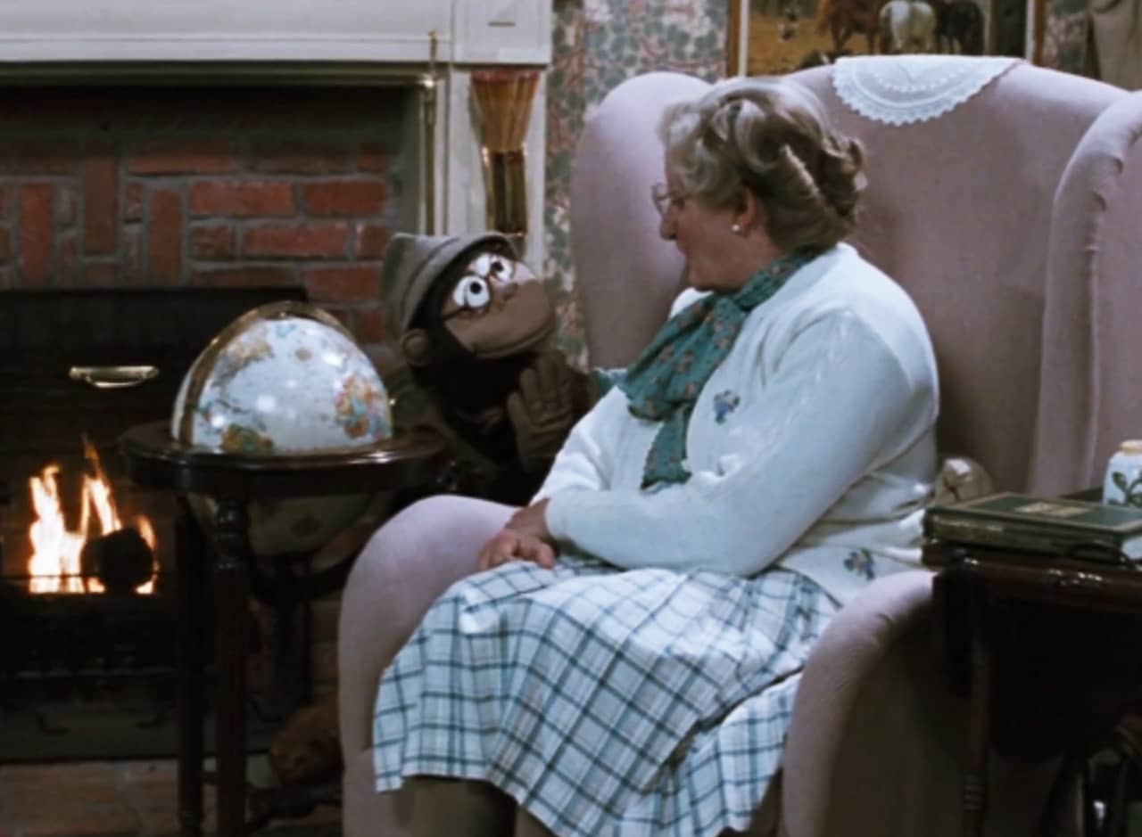 Euphegenia, a nice elderly English woman, sits in her living room looking at a globe with a chimp puppet