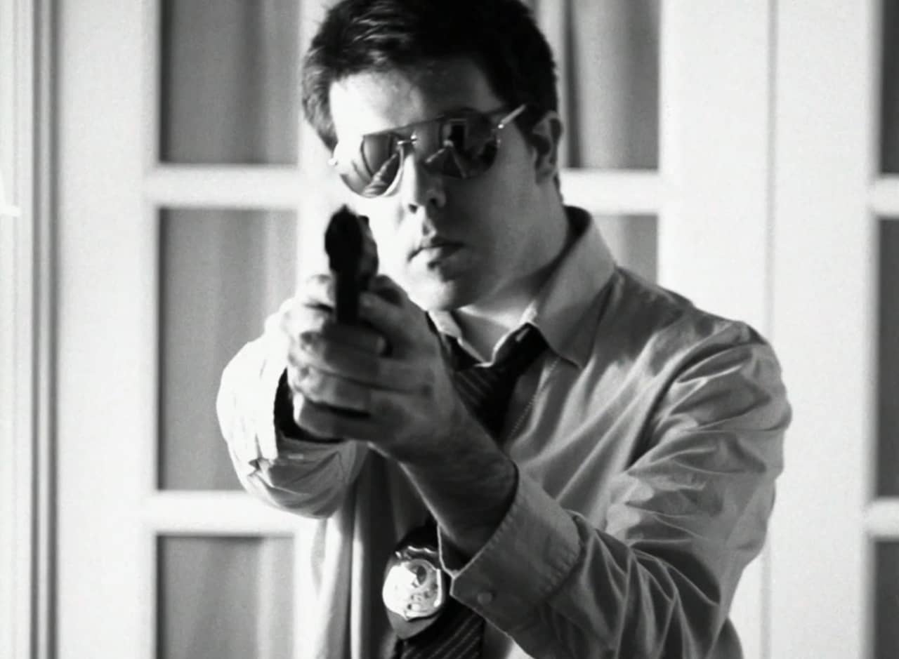 black and white photo of a police detective wearing aviators and pointing a gun