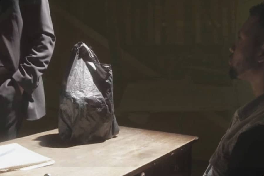 black man sitting at an interrogation table with a plastic bag of stuff