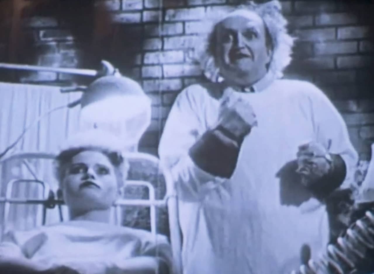 Dr. Frankenstein, a mad scientist, next to a woman on an experiment table