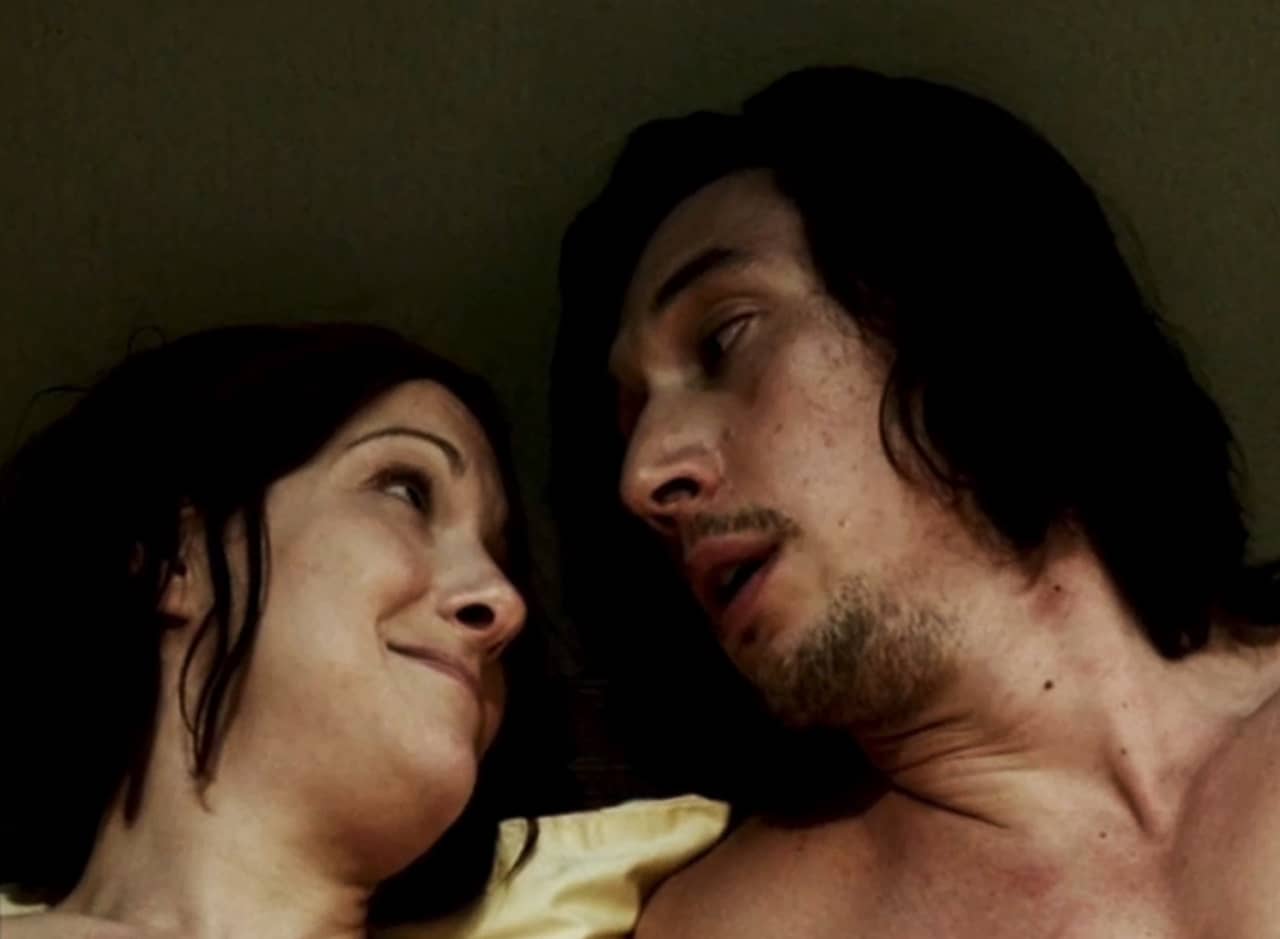 Adam and Mira in bed, looking at each other