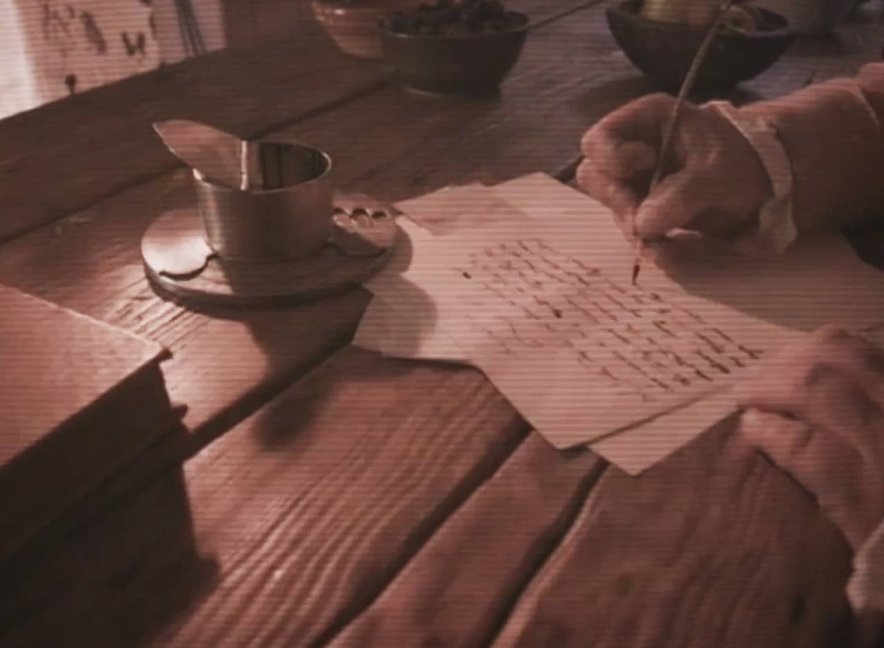 old timey desk with a man writing a letter with a quill and ink
