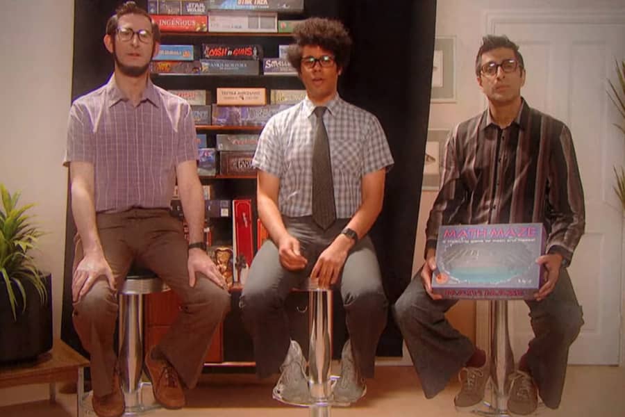 Maurice, Newton, and Booth sitting on tall stools in front of a shelf of board games