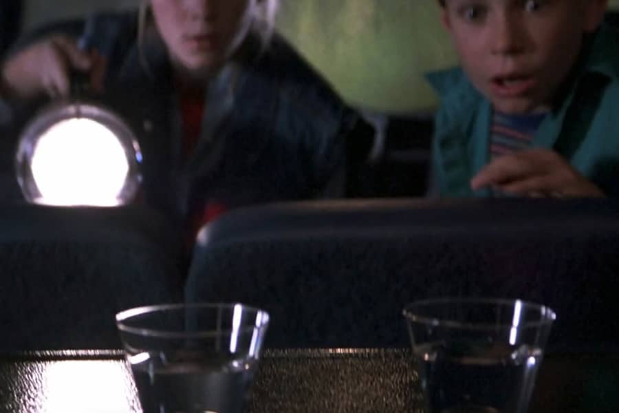 two kids shine a flashlight at two cups of water