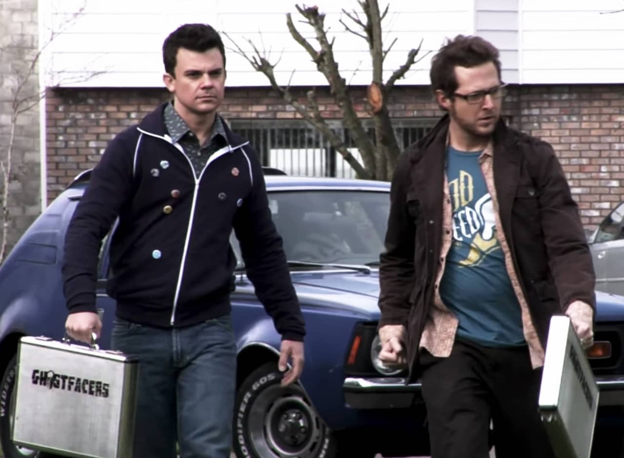 two young dudes, Harry and Ed, walk with Ghostfacers brief cases