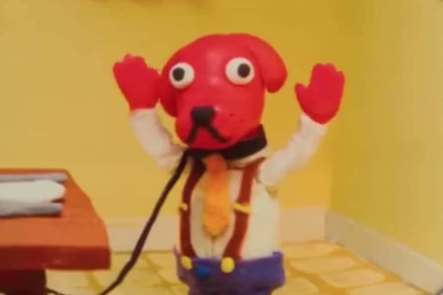red dog wearing a tie and suspenders holds his hands in the air