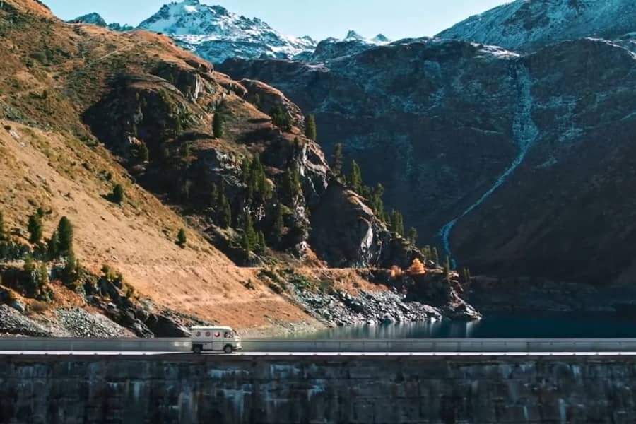 cheese delivery truck driving over a dam bridge with mountains behind