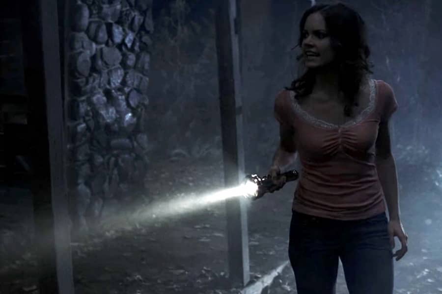 the young brunette shines a flashlight in a creepy abandoned cabin