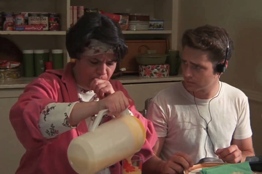 a mom coughs as she pours juice at the breakfast table with her teen son