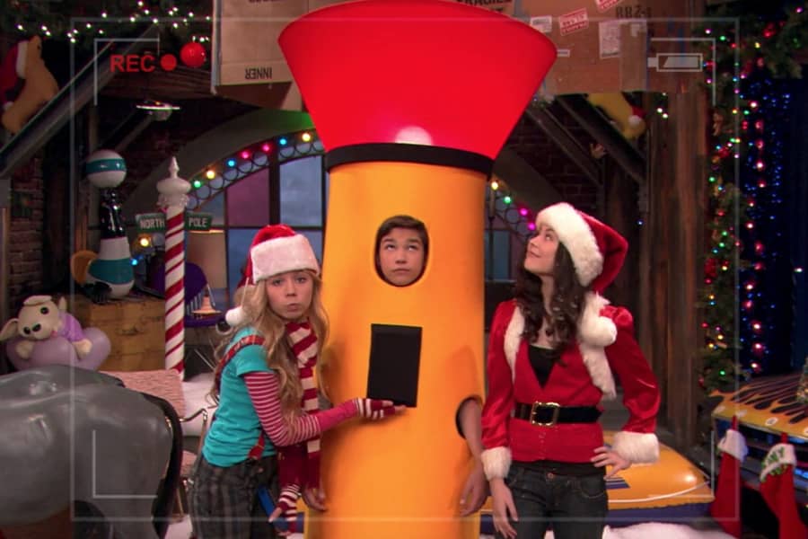 Sam and Carly dressed in Santa hats with Freddie dressed as a giant flashlight