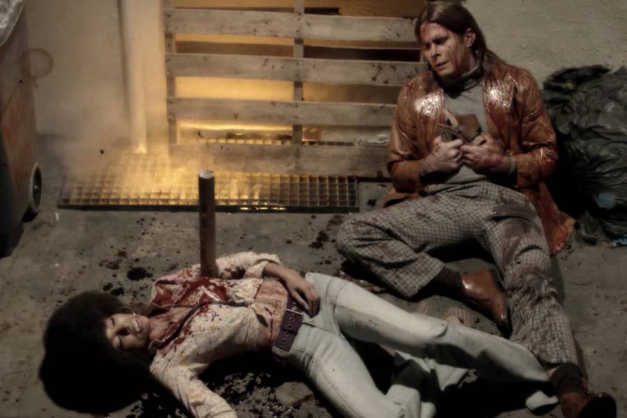 Rocky, covered in blood, sits distressed next to a dead Cindy