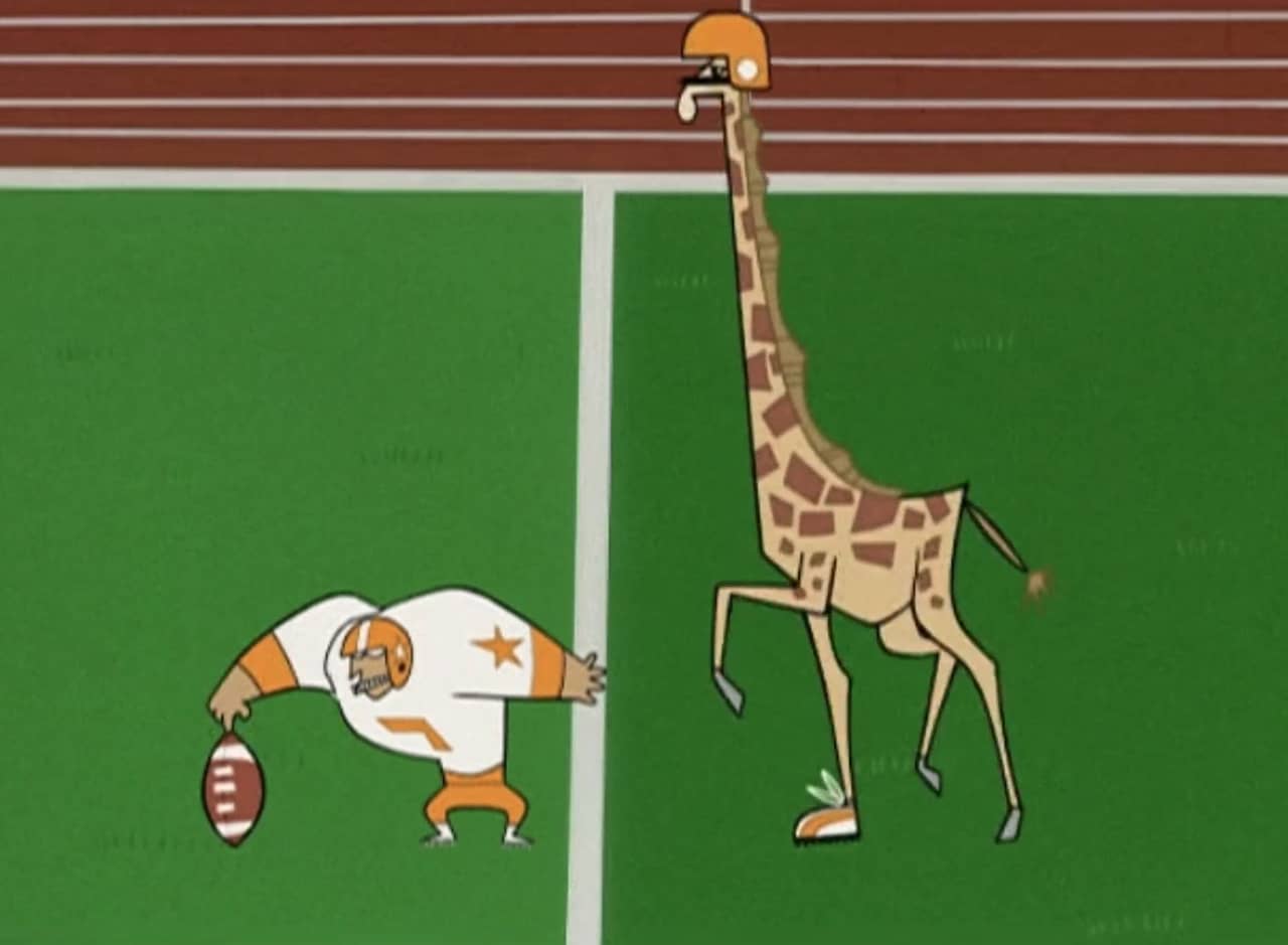 a giraffe runs to kick a football held by his teammate