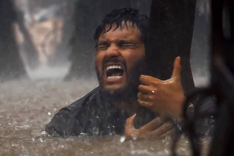 Jack Mimoun in chest-deep water, gripping a tree in the rain