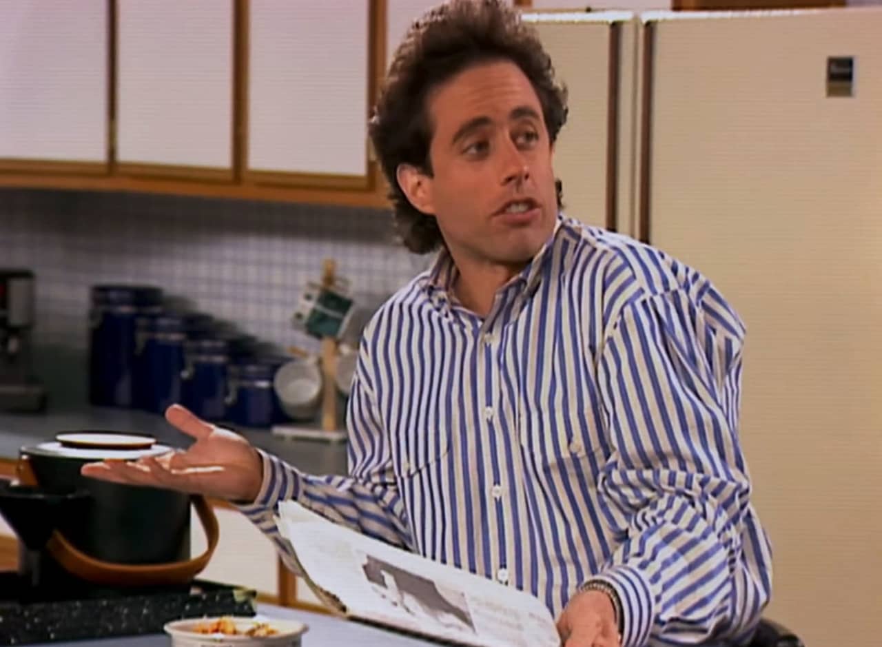 Jerry Seinfeld shrugging in his apartment kitchen