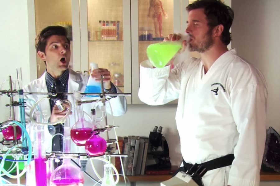 Johnny drinking a neon green liquid from a science flask as Ben Wyatt yells
