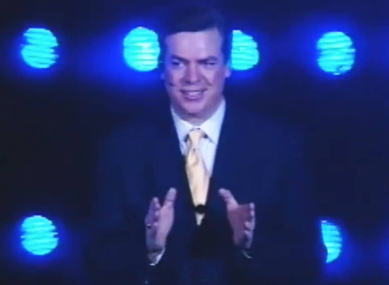 Tappy Tibbons in a suit giving a talk in front of blue lights