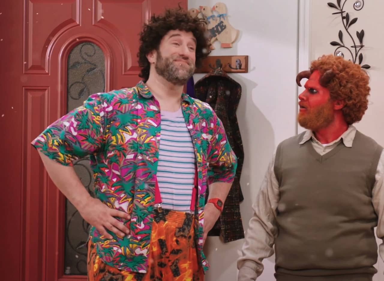 Dustin Diamond as Squeak, wearing colorful patterned shirt and pants, next to a demon dressed in a sweater vest