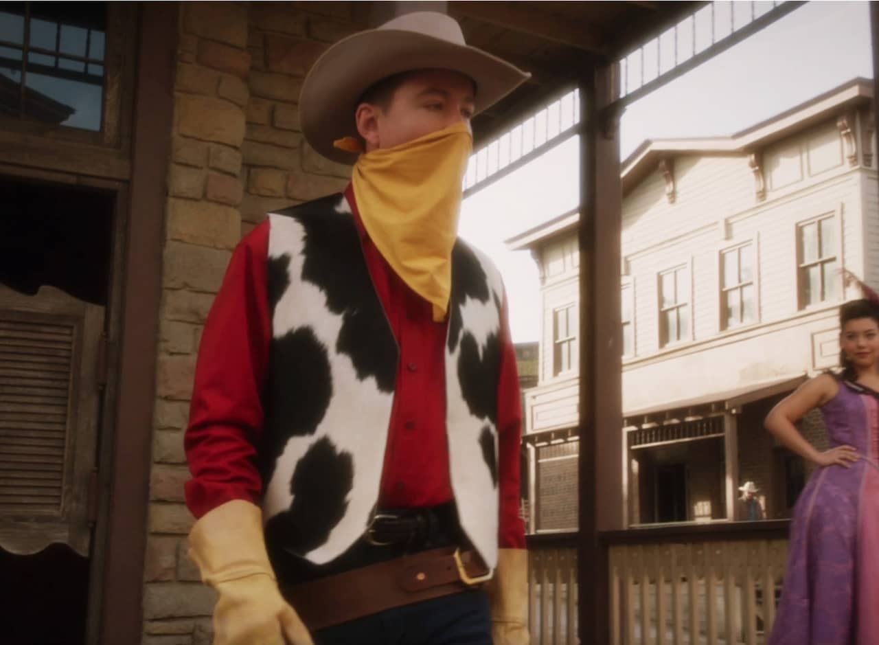 Kid Colt, a cowboy in a red shirt, cow-patterned vest, yellow gloves, and yellow bandana covering his face