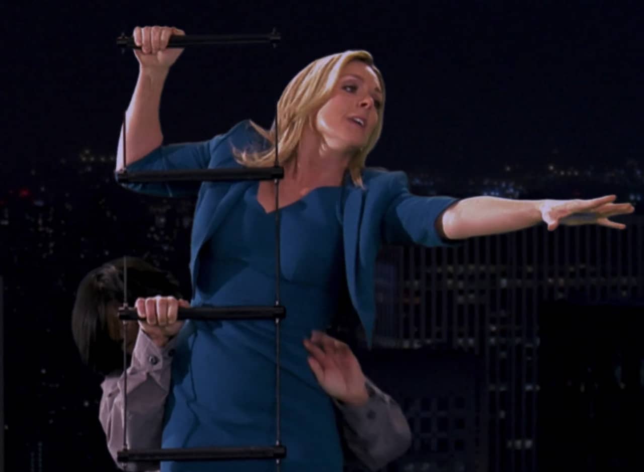 Jenna Maroney as Jessup, reaching out as she is force up a helicopter dangling ladder