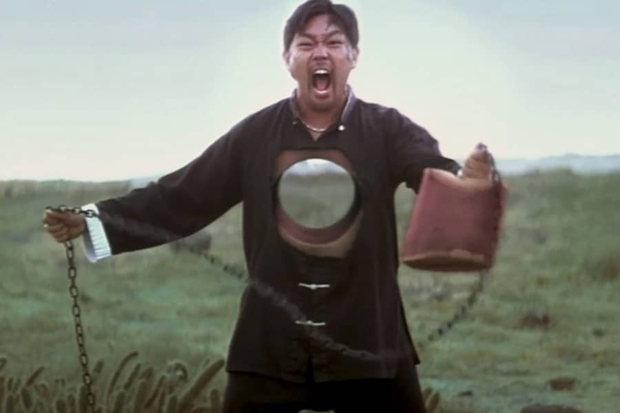 a man screams as he holds a cylindrical object with a long chain; a cylindrical hole in his torso shows the landscape behind him