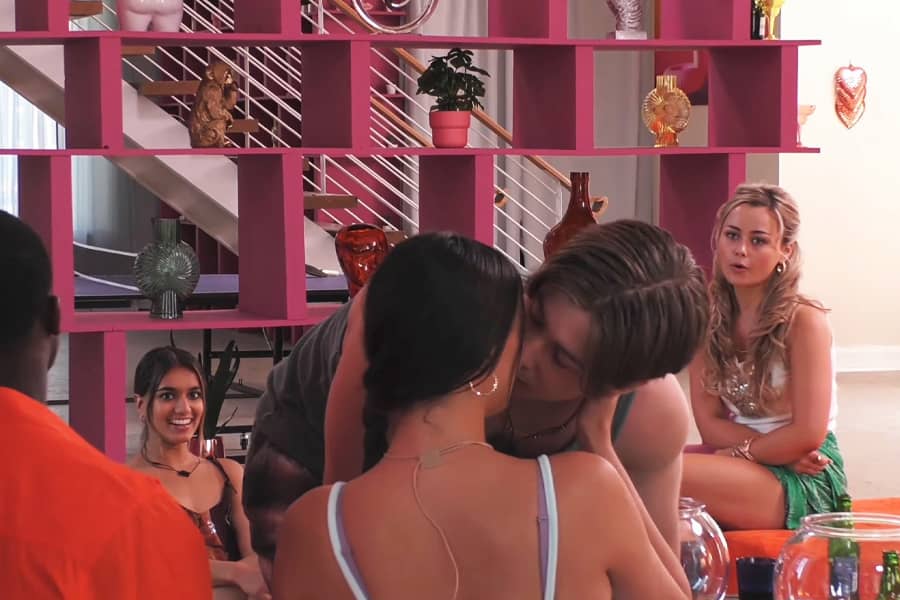 tank top guy kisses a woman while others watch