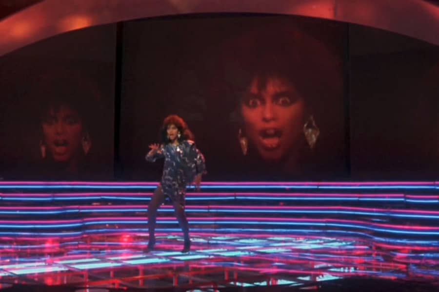 Laura Charles dancing on stage, her face big on the screen behind her