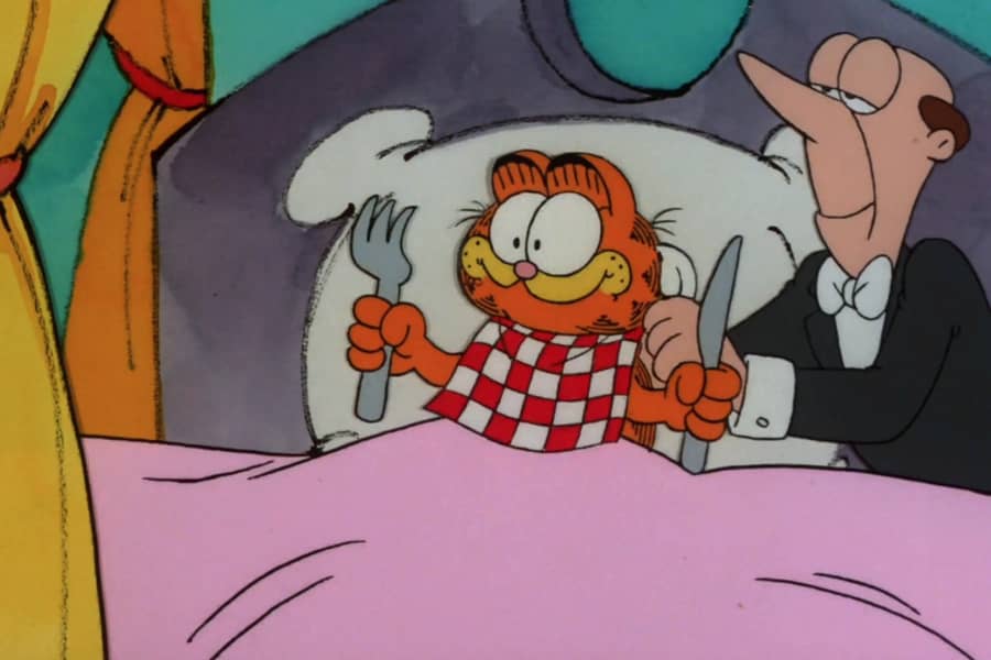 Garfield in bed holding a knife and fork, a butler is tying a napkin to his chin