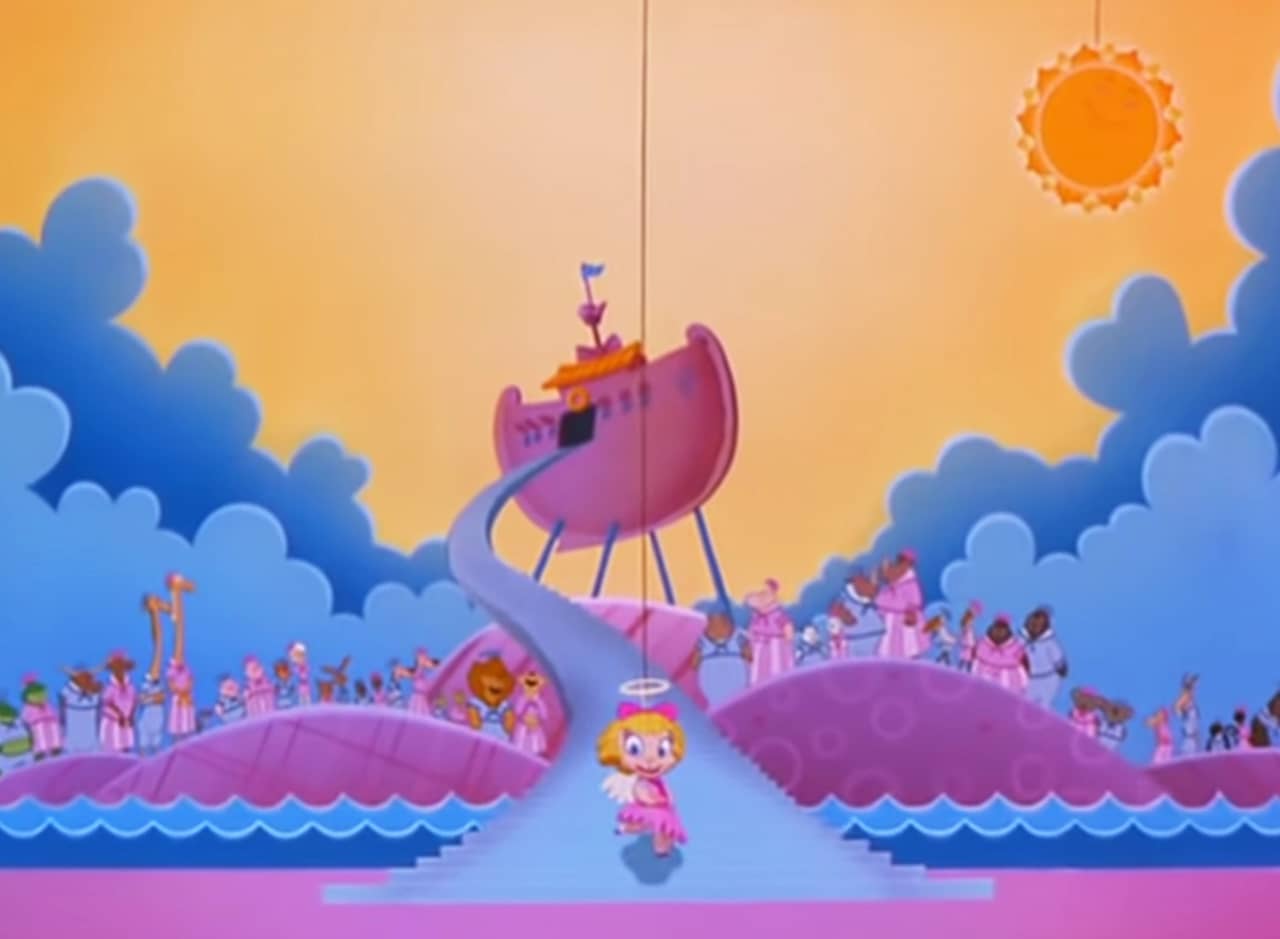 Darla Dimple, a young girl with golden curly hair, is dressed as an angel and approaches a pink and blue set depicting Noah’s ark