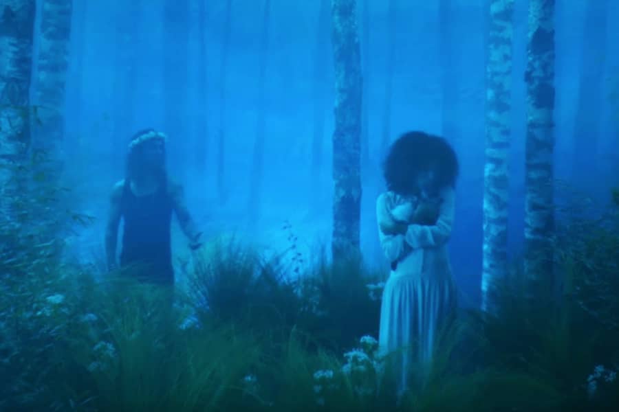 man approaches woman in a foggy forest, she is holding a baby goat