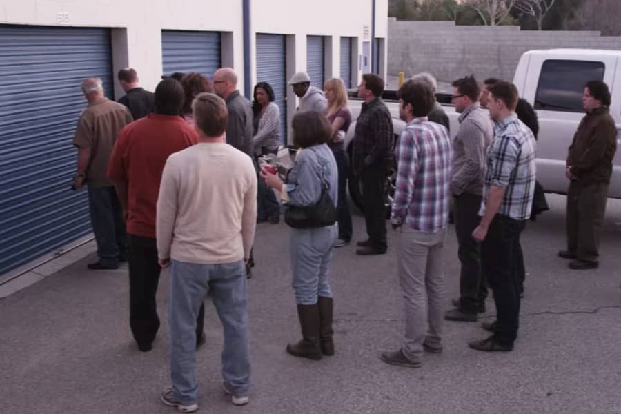 people stand around outside a storage locker waiting for it to be opened