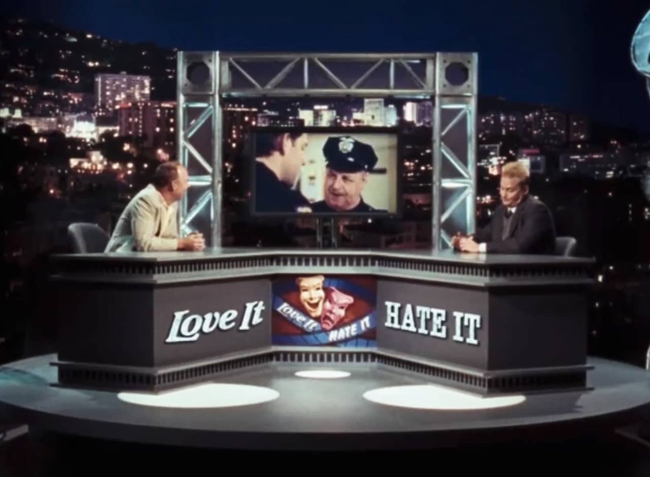 a talk show set with Ben Lilly across from David van Zyverdan and a television between them